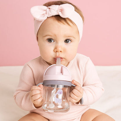 bébé boit avec un verre pour bébé rose