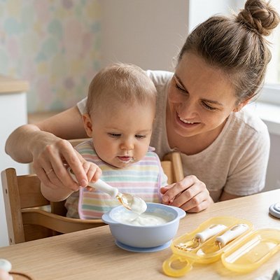 Maman aide sons bébé à manger avec un couvert pour bébé ​